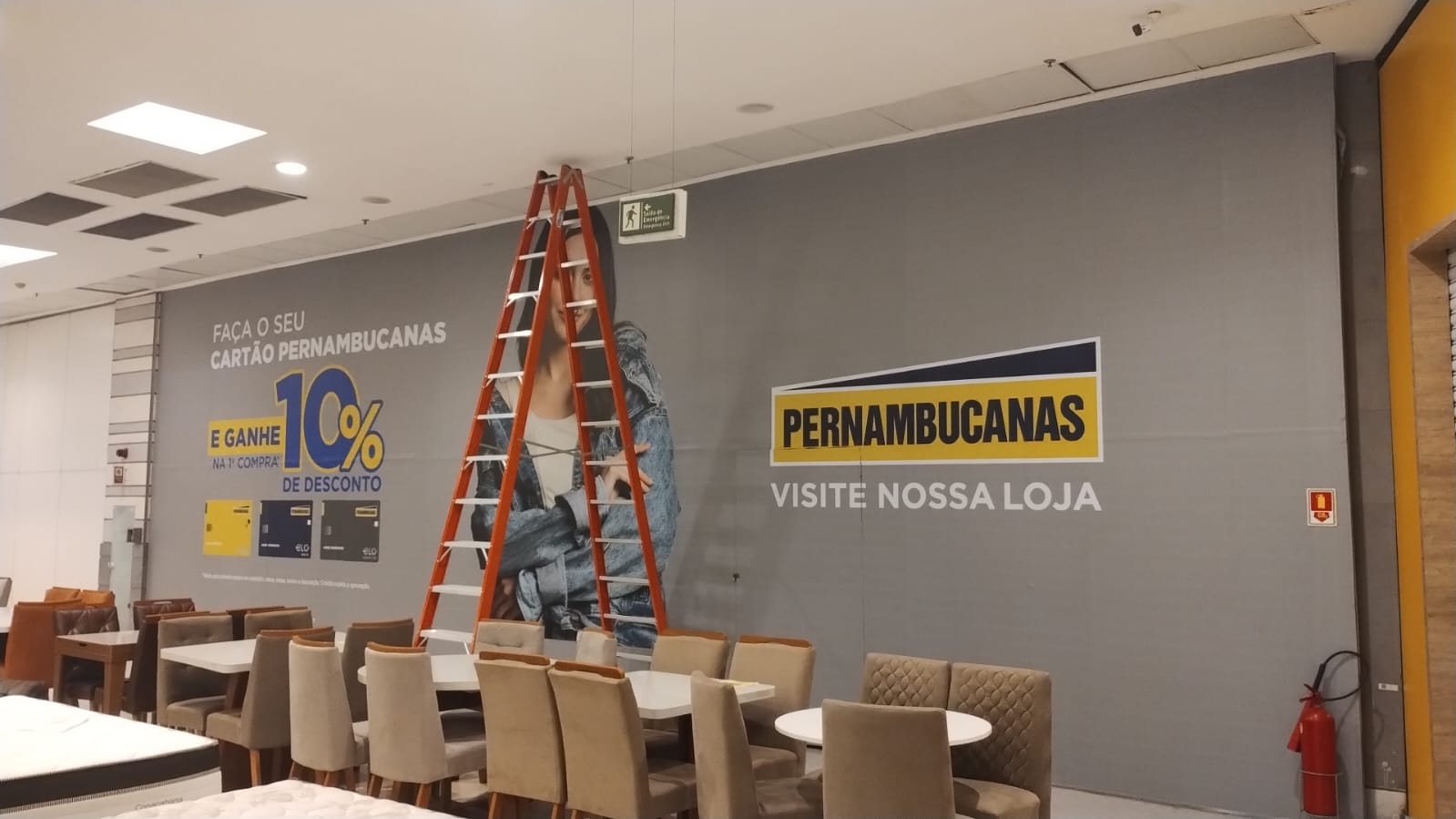 Tapume da Pernambucanas instalado em corredor de shopping, com a chamada Visite Nossa Loja
